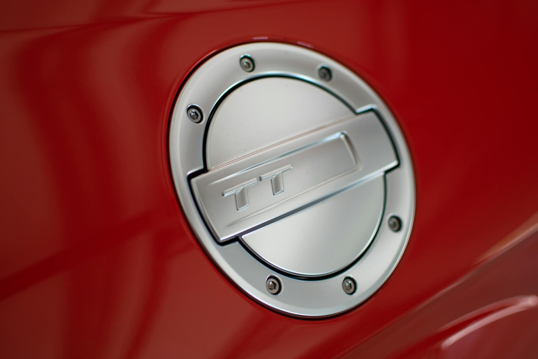 Detailed view of a shiny metallic fuel cap on a red sports car, showcasing automotive design.